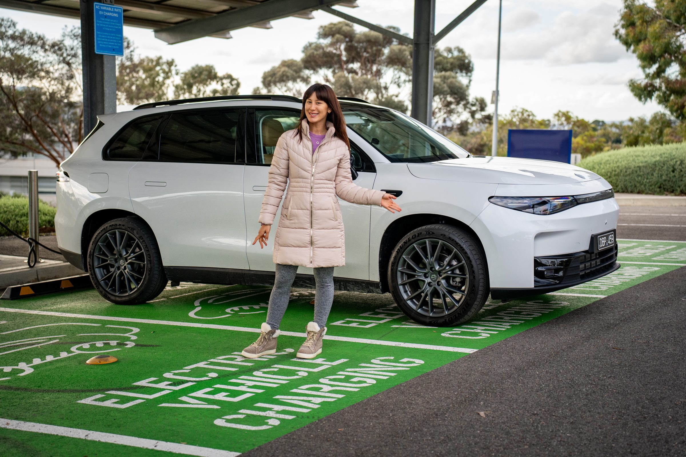 A cartell.live presenter with an electric vehicle at a charging bay